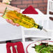 A hand pours Tablecraft olive oil into a plate of salad.