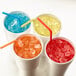 A group of cups of different colored drinks with ice and straws.