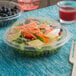 A salad in a Dart PET16BDL plastic bowl with a fork and knife on a table.
