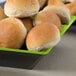 A green and black square melamine bowl filled with bread rolls.