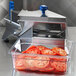 An Edlund tomato slicer on a counter with a container of sliced tomatoes.