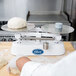 A person using an Edlund stainless steel baker's dough scale to weigh dough.