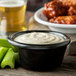 A Carlisle black melamine ramekin filled with white sauce on a platter with celery sticks and wings.