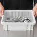 A person holding a plastic Metro clear tote full of silverware.