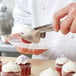 A person using Carlisle stainless steel pastry tongs to pick up a cupcake with white frosting.