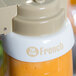 A Tablecraft white plastic dispenser collar with beige lettering over a container of orange liquid.