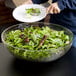 A person holding a plate with a salad in a Cambro clear ribbed bowl.