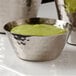 An American Metalcraft stainless steel round sauce cup filled with green sauce on a table.