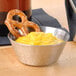 A stainless steel sauce cup filled with yellow liquid next to pretzels.