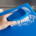 A hand using a blue brush with white bristles to clean a blue cutting board.