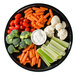 A WNA Comet black round catering tray with a plate of carrots and broccoli, baby carrots, tomatoes, and a bowl of white dip.
