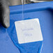 A square dissolving product label with handwritten text on a blue container being exposed to water.