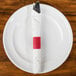 A red napkin wrapped around a fork on a white plate.