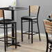 A Lancaster Table & Seating black bistro bar stool with black vinyl seat and natural wood back on a table in a restaurant dining area.