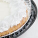 A pie with white frosting on top in a black plastic container with a clear lid.