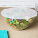 A Fineline clear plastic bowl filled with salad with a plastic lid on top.