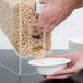 A person pouring cereal from a Choice dry food dispenser into a bowl.