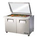 A True stainless steel refrigerated sandwich prep table with hinged glass lids on a counter.