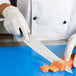 A person wearing a white glove uses a Mercer Culinary MX3 Sujihiki knife to cut salmon on a blue surface.