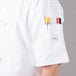 A person wearing a white Mercer Culinary chef jacket with a pocket full of pens and a knife.