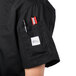 A person wearing a Mercer Culinary black short sleeve chef jacket with a pen in the pocket.
