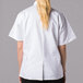 A woman wearing a Mercer Culinary white short sleeve chef jacket with cloth knot buttons.