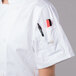 A person wearing a Mercer Culinary white chef jacket with a pen in the pocket.