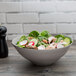 A 10 Strawberry Street matte gray stoneware bowl filled with salad with mushrooms, radishes, and other vegetables.