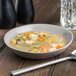 A close-up of a gray 10 Strawberry Street RPPLE soup bowl filled with chicken and vegetable soup.