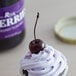 A cupcake with purple frosting and a Regal Maraschino cherry with a stem on top.