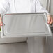 A chef holding a Vollrath stainless steel tray cover over food on a counter.