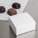 A white 2 1/2" x 2 1/2" candy box with chocolates on top.