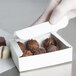A gloved hand holding a white 1/4 lb. candy box filled with chocolates.