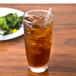 A Libbey customizable cooler glass of iced tea with a straw next to a plate of salad.