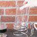 A hand holding a Libbey glass container pouring coffee into a French press.