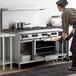 A man wearing a chef's hat using a Garland 8 burner range with oven and storage base to cook food.
