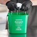 A person in black gloves washing a green Noble Products cleaning pail.