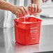 A person washing a red pail with a sponge.