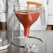 A Matfer Bourgeat polycarbonate automatic dispenser funnel pouring liquid into a glass.