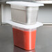 A white Flexsil lid on a stack of plastic containers filled with red sauce.