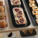 A black Cambro market tray of pastries on a bakery display counter.