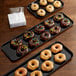 A Cambro black fiberglass market tray with chocolate donuts topped with candy displayed on a counter.