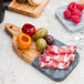 An American Metalcraft olive wood and black marble serving board with meat and fruit on it.