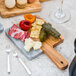 An American Metalcraft olive wood and gray marble serving board with food on it.