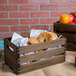 An American Metalcraft wooden crate with bagels and apples on a table.