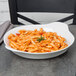A Libbey Aluma White Porcelain bowl filled with pasta and tomato sauce on a table.