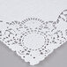 A white floral lace paper placemat on a gray surface.