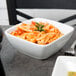 A Libbey white porcelain square bowl filled with pasta and sauce with a fork.