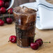 A Carlisle clear plastic tumbler of soda with ice and cherries.