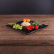 An Elite Global Solutions faux black slate melamine serving board with vegetables on a wood table.